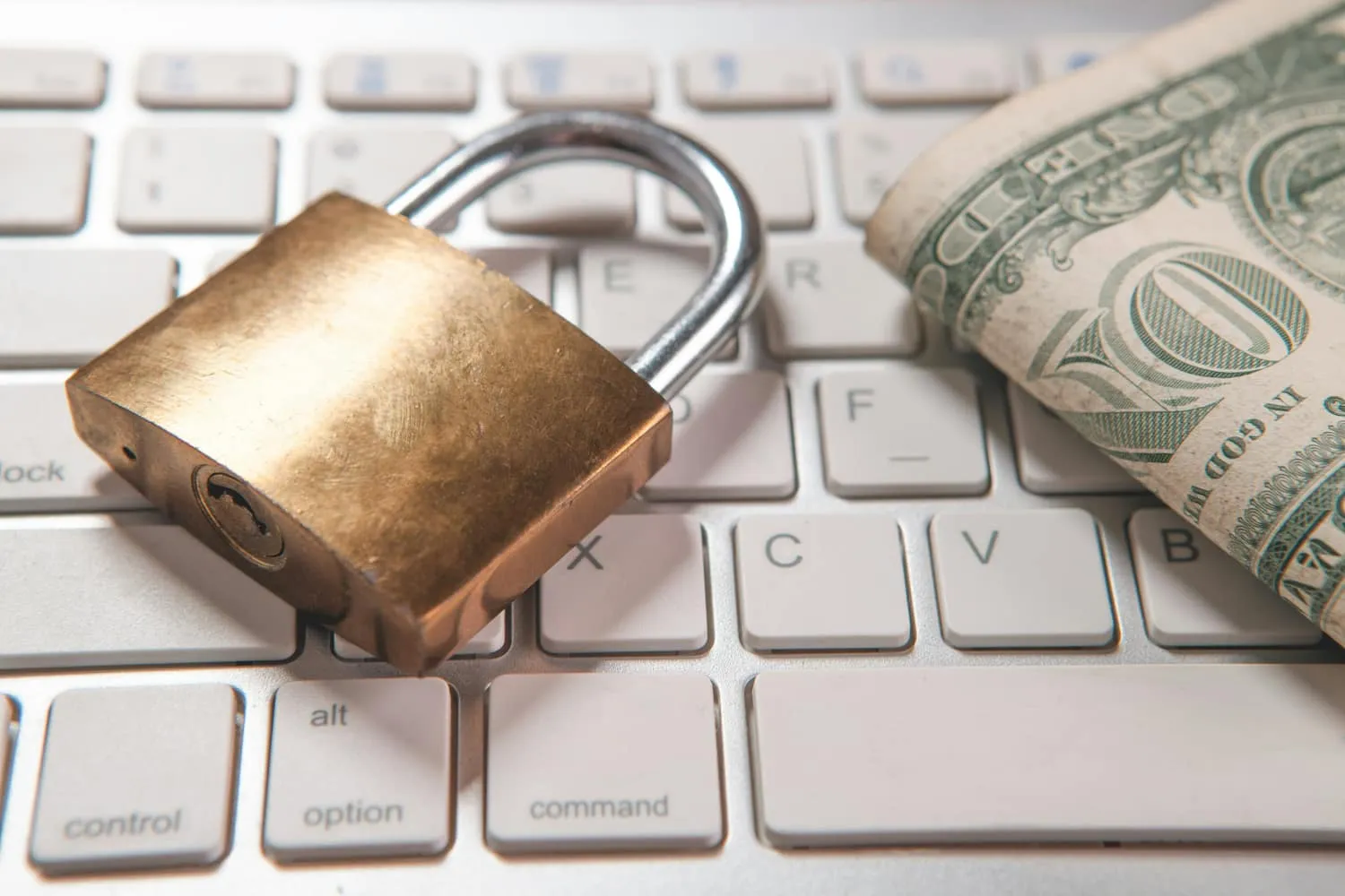 A brass padlock and a rolled-up banknote resting on a computer keyboard.