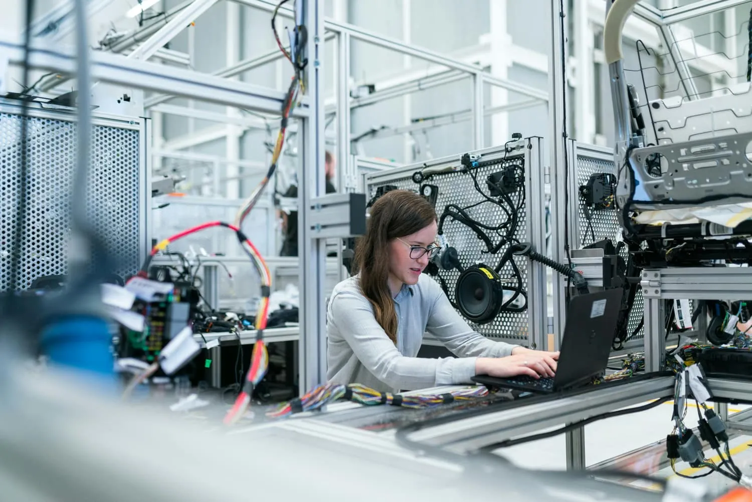 An engineer working on a laptop beside a wiring harness assembly rig in an electronics manufacturing facility.