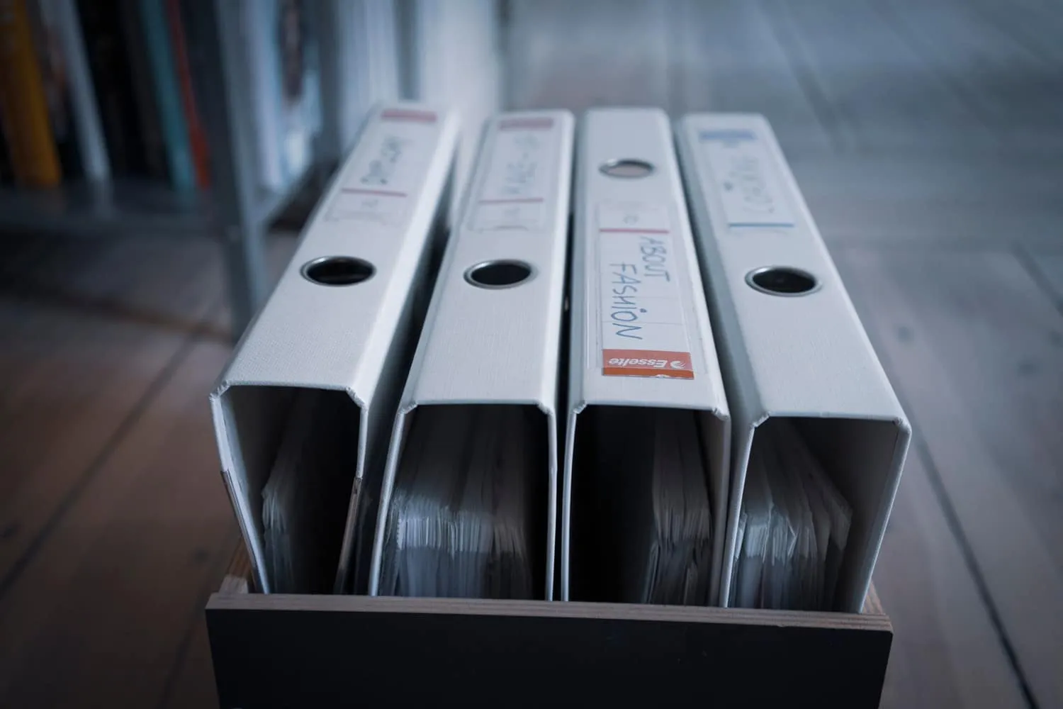 Four white ring binders standing upright in a wooden crate, their spines hand-labelled — the physical evidence pack an auditor actually reads.