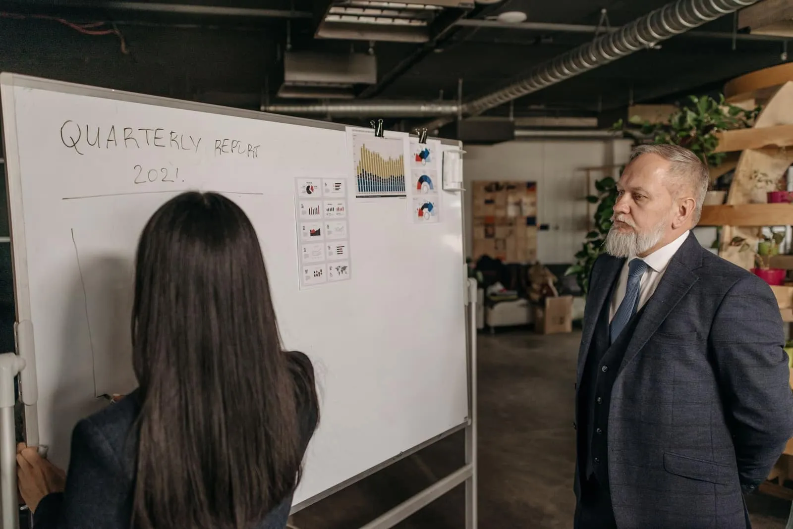 A senior advisor watches a colleague walk through a quarterly review at a whiteboard — the kind of milestone review where a board holds its vCISO to account.